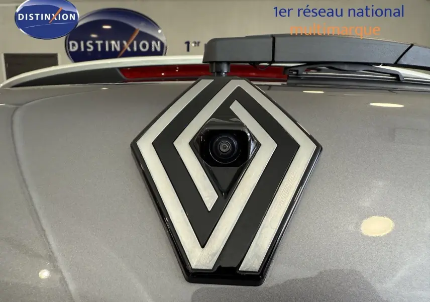 Gros plan sur le logo Renault gris avec caméra intégrée, sur le capot gris cassiopée métallisé du Captur 2025.