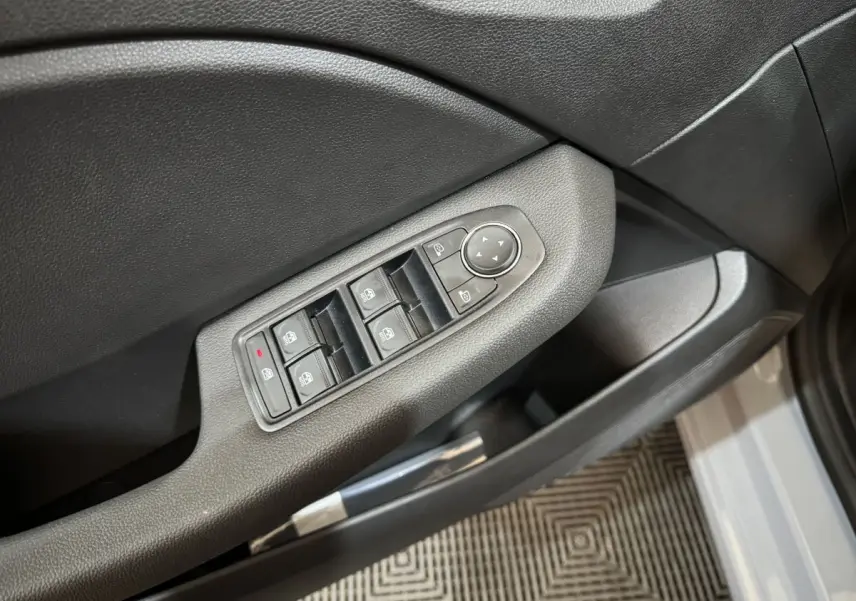 Gros plan sur les commandes des vitres et rétroviseurs côté conducteur d'une Renault Clio gris clair 2025.