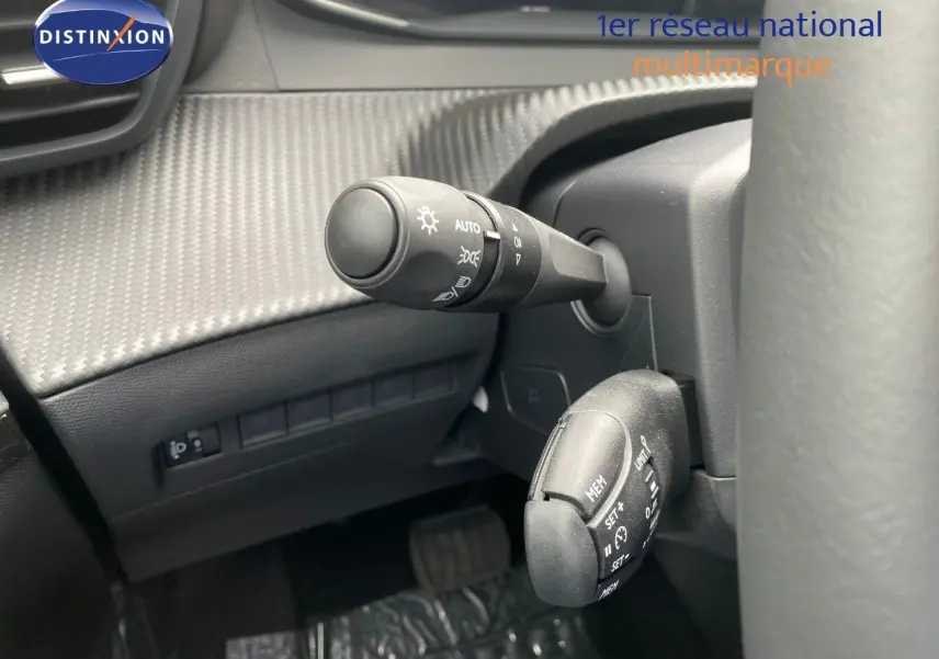 Détail intérieur du combiné de commandes au volant d’une Peugeot 208 gris sélénium, mettant en valeur les commandes d’éclairage et de régulateur.