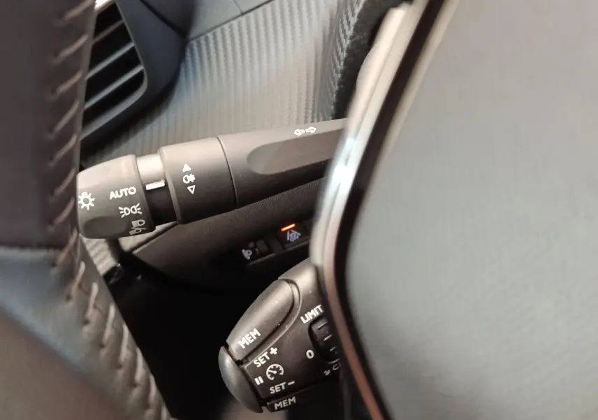 Gros plan sur la commande multifonctions noire du volant d'une Peugeot 208 2023, intérieur gris et noir.