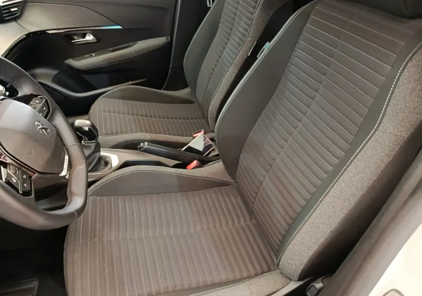 Vue intérieure côté conducteur de la Peugeot 208 2023, sièges tissu gris et volant cuir multifonctions noir.