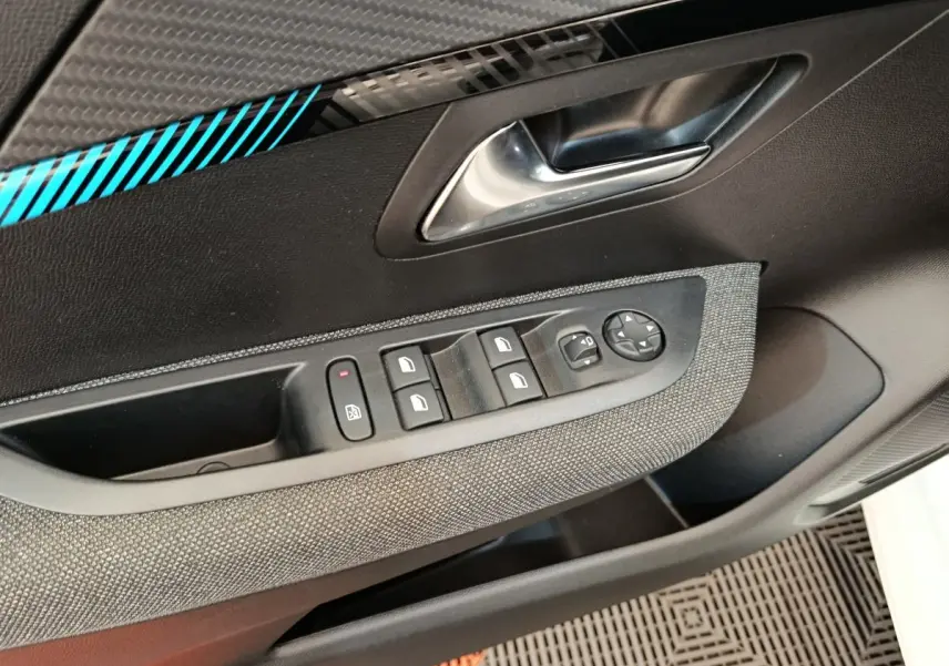 Gros plan sur la porte côté conducteur de la Peugeot 208 2023, montrant les commandes des vitres et le décor carbone avec liseré bleu.