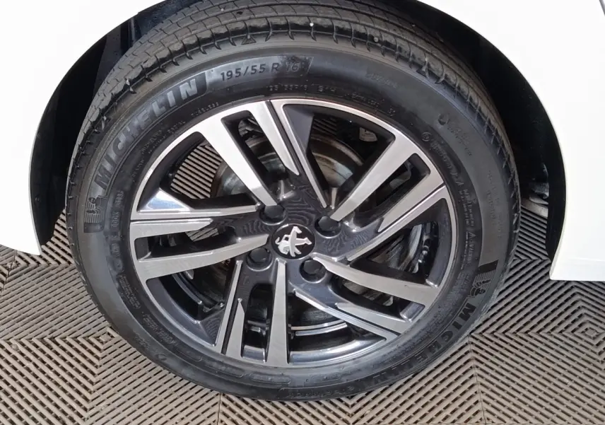 Gros plan sur la roue avant droite d'une Peugeot 208 blanche avec jante alliage bicolore et logo lion au centre.