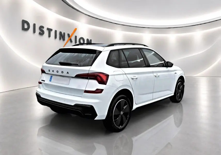 Vue 3/4 arrière droite d'un Skoda Kamiq blanc nacré avec jantes noires et toit noir dans un showroom lumineux.