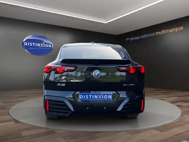 Vue arrière d'un BMW X2 sDrive20d M Sport noir, avec feux LED et logo distinctif sur fond showroom.