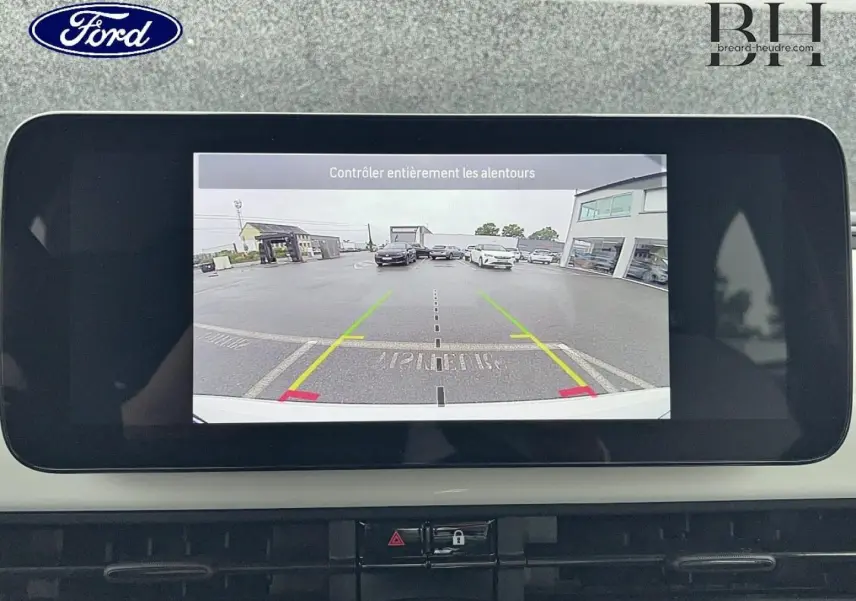 Écran de caméra de recul dans une Ford, affichant une vue arrière sur un parking avec plusieurs voitures visibles.
