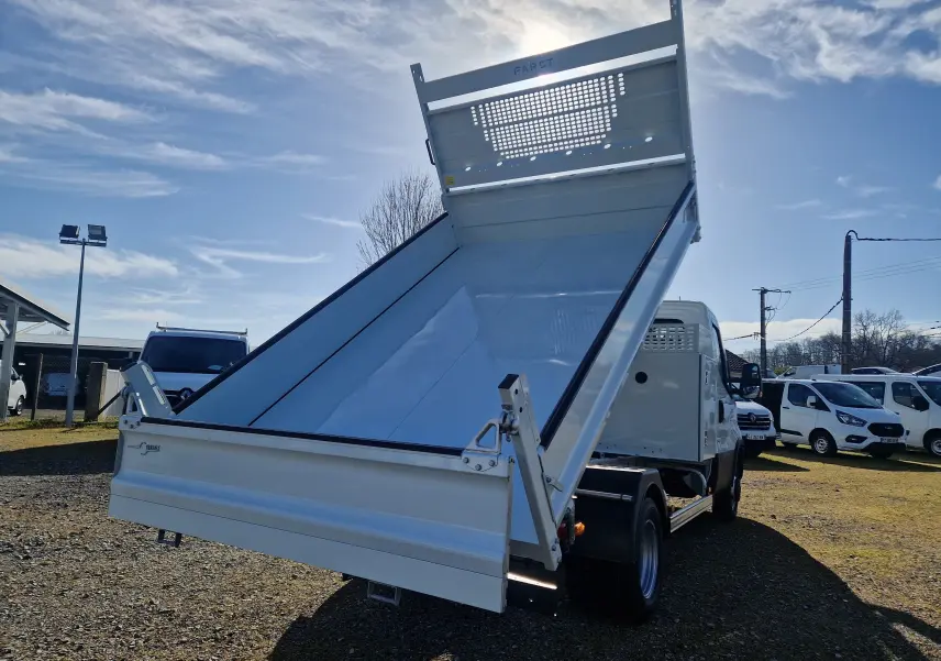 Vue arrière en léger contre-plongée d’un Iveco Daily blanc avec benne acier relevée et coffre latéral visible.