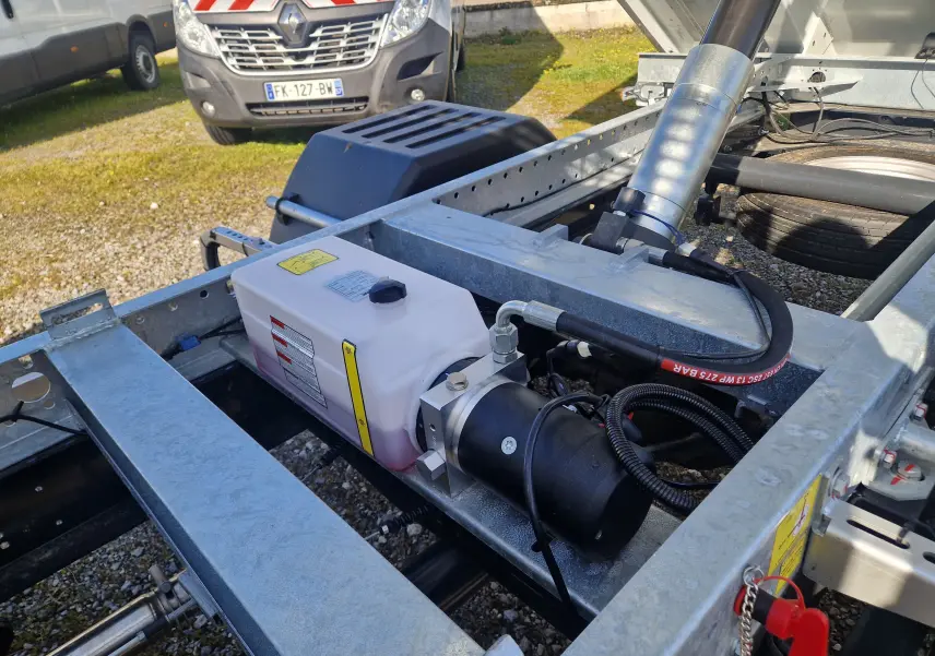 Gros plan sur le châssis métallique gris et le système hydraulique du benne blanc Iveco Daily 35C16, vue arrière droite.