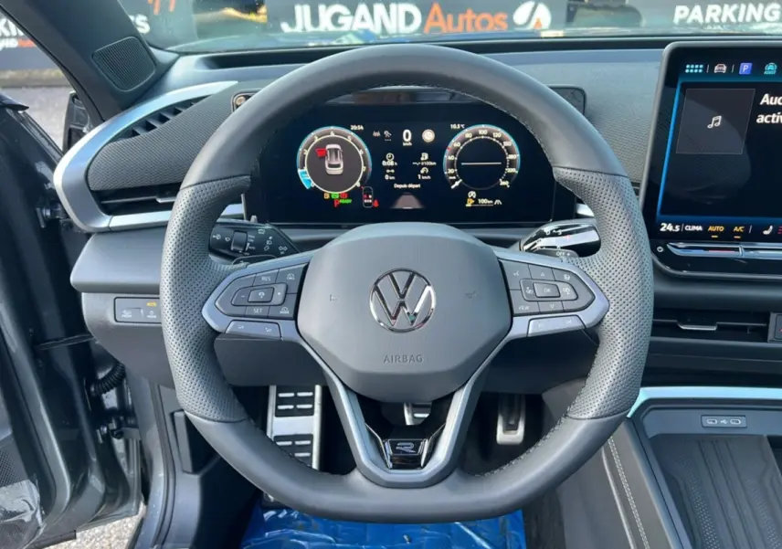 Vue intérieure centrée sur le volant cuir multifonctions du Volkswagen T-Roc gris loup avec tableau de bord digital et écran tactile.