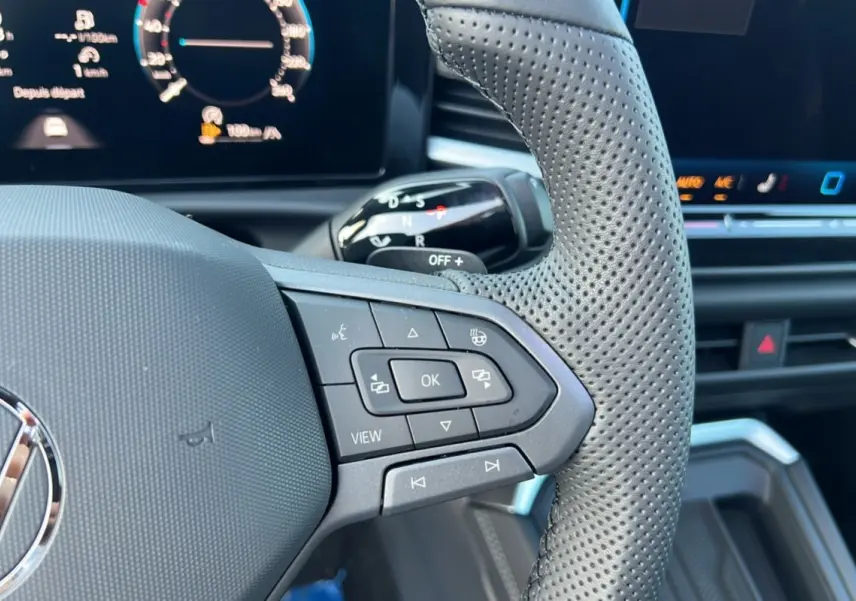 Gros plan sur le volant cuir perforé multifonctions côté droit du Volkswagen T-Roc gris loup avec tableau de bord digital.