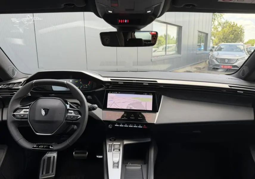Vue intérieure avant du Peugeot 308 NV Hybrid 145 GT e-DSC6 2026, tableau de bord noir avec écran tactile central et volant GT cuir.