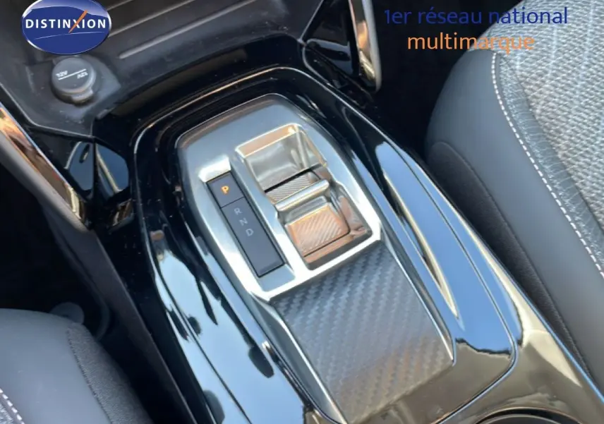 Gros plan sur la console centrale noire laquée de la Peugeot 208 Hybrid 110ch, avec levier de boîte automatique et finition carbone.