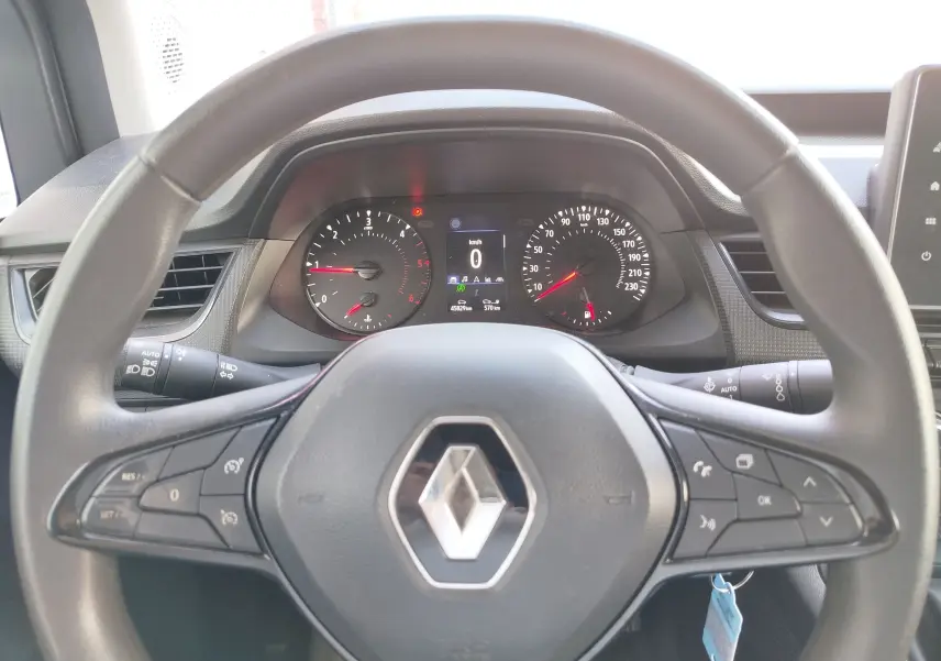 Vue rapprochée du volant Renault et du tableau de bord numérique du Kangoo blanc, avec commandes multifonctions visibles.