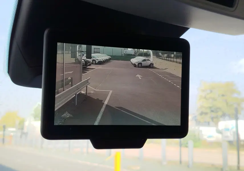 Vue de l'écran de caméra de recul du Renault Kangoo 2023 montrant un parking avec plusieurs véhicules blancs.