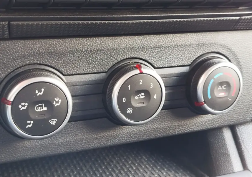 Gros plan sur les commandes de climatisation noires et argentées du Renault Kangoo 2023, avec réglages de ventilation et air conditionné.