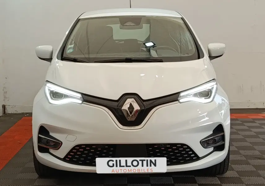 Vue frontale d'une Renault ZOE Intens R110 blanche avec phares LED allumés et calandre noire distinctive.