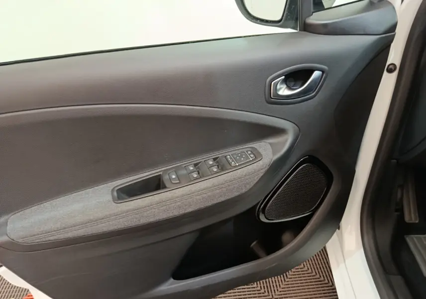 Vue intérieure côté gauche de la porte avant blanche de la Renault ZOE Intens avec commandes électriques et haut-parleur intégré.