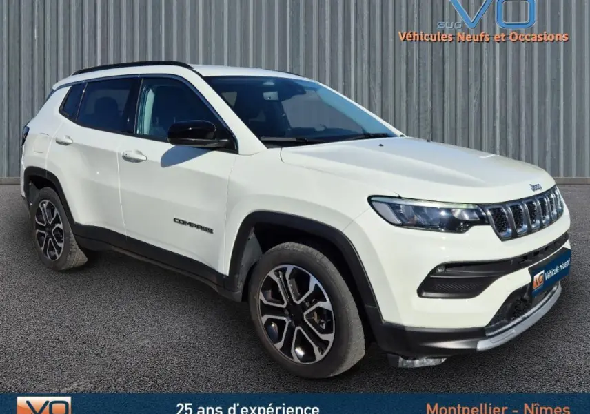 Vue 3/4 avant droit d'un Jeep Compass blanc avec barres de toit et jantes 18 pouces, sur fond industriel.
