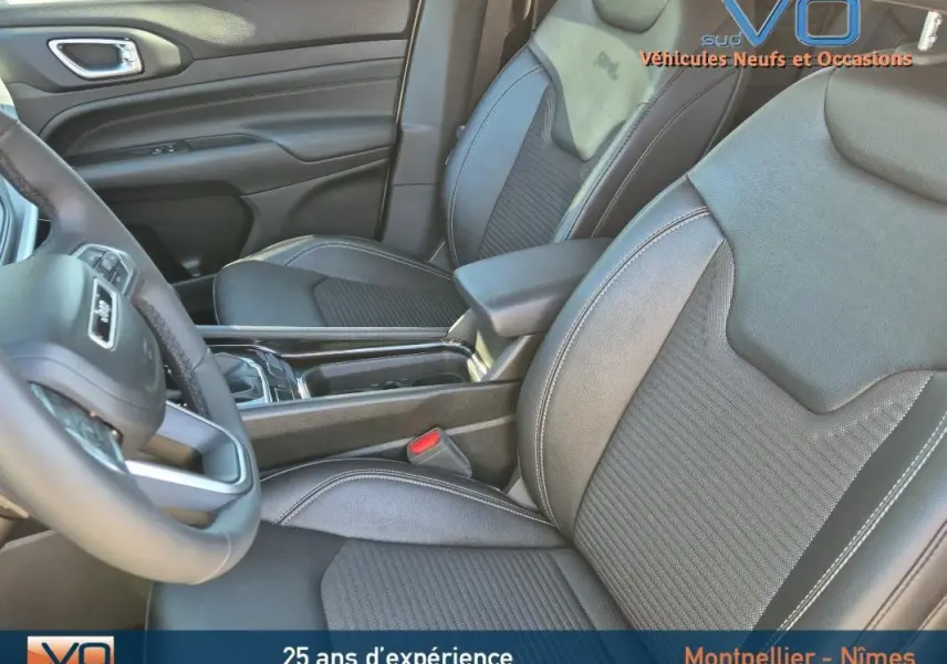 Vue intérieure rapprochée des sièges avant en cuir noir du Jeep Compass 2023 avec accoudoir central et volant partiel visible.