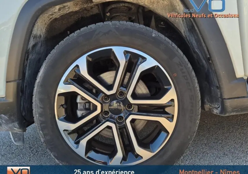 Gros plan sur la jante 18 pouces bicolore noir et argent du côté avant droit du Jeep Compass blanc 2023.