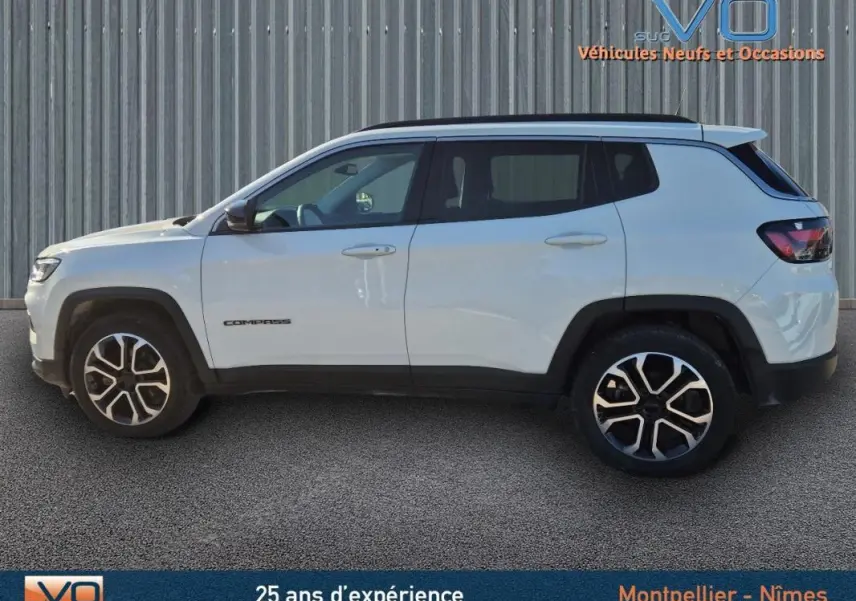 Vue de profil côté gauche d'un Jeep Compass blanc 2023 avec jantes 18 pouces et barres de toit noires.