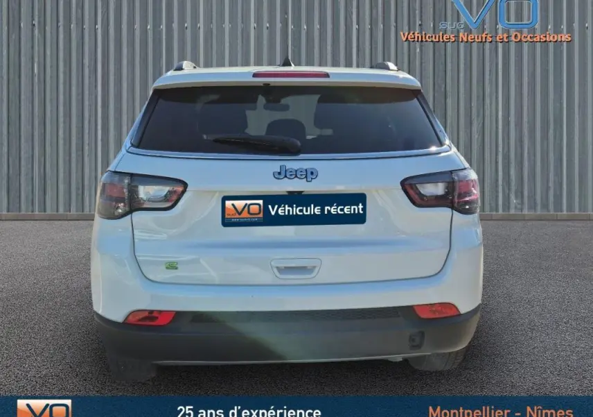 Vue arrière d'un Jeep Compass blanc 2023 avec feux arrière fumés et barres de toit visibles.