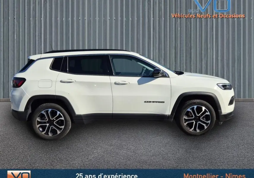 Vue de profil côté gauche d'un Jeep Compass blanc 2023 avec jantes 18 pouces et barres de toit noires.