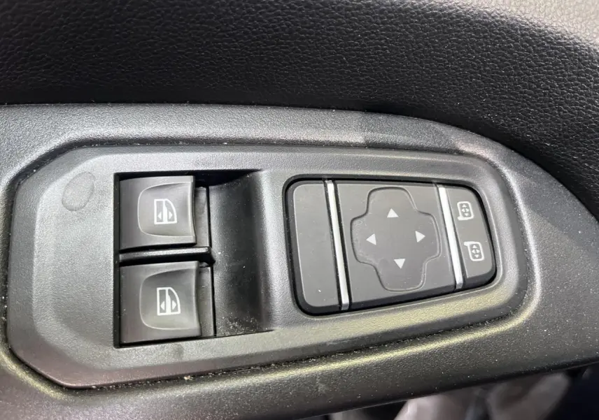 Gros plan sur les commandes de lève-vitres et réglage des rétroviseurs du Renault Trafic Fourgon gris foncé.