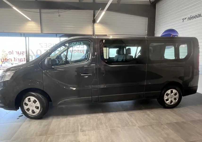 Vue de profil côté gauche du Renault Trafic Fourgon gris foncé avec vitres teintées et jantes 16 pouces en intérieur showroom.