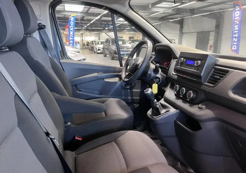 Vue intérieure côté conducteur du Renault Trafic Fourgon 2023, montrant sièges tissu gris et tableau de bord fonctionnel.