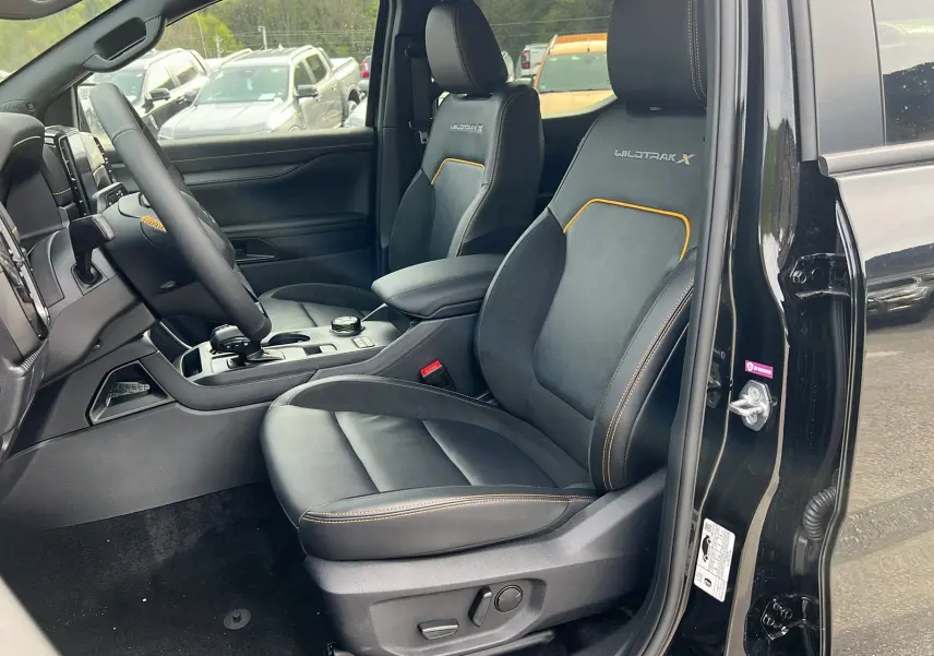 Vue intérieure côté conducteur du Ford Ranger Wildtrak X noir agate, sièges en cuir avec surpiqûres orange et logo Wildtrak X brodé.