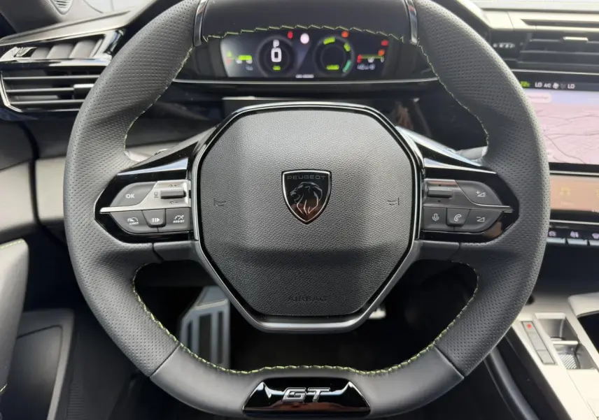Vue rapprochée du volant compact GT en cuir noir avec surpiqûres vert Adamite et logo Peugeot au centre.