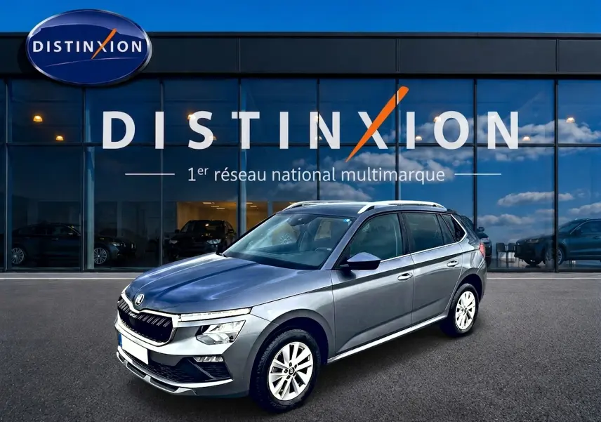 SKODA KAMIQ gris en 3/4 avant droit, avec calandre chromée et barres de toit blanches visibles.