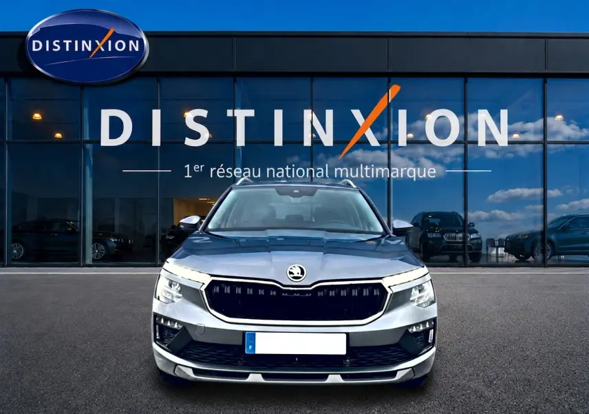 Vue de face d'un Skoda Kamiq gris 2025 avec calandre noire et barres de toit devant une vitrine Distinxion.