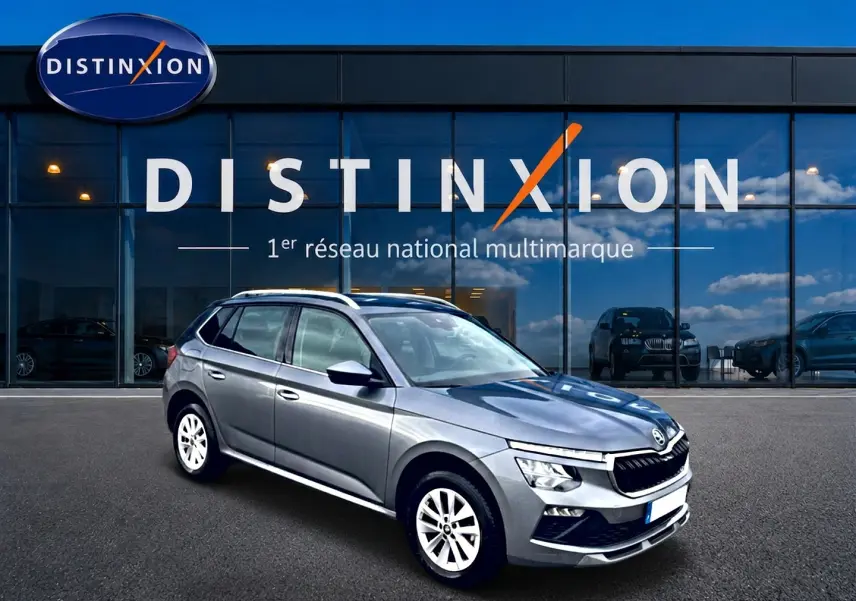 Vue 3/4 avant droit d'un Skoda Kamiq gris métallisé devant une vitrine avec logo Distinxion.