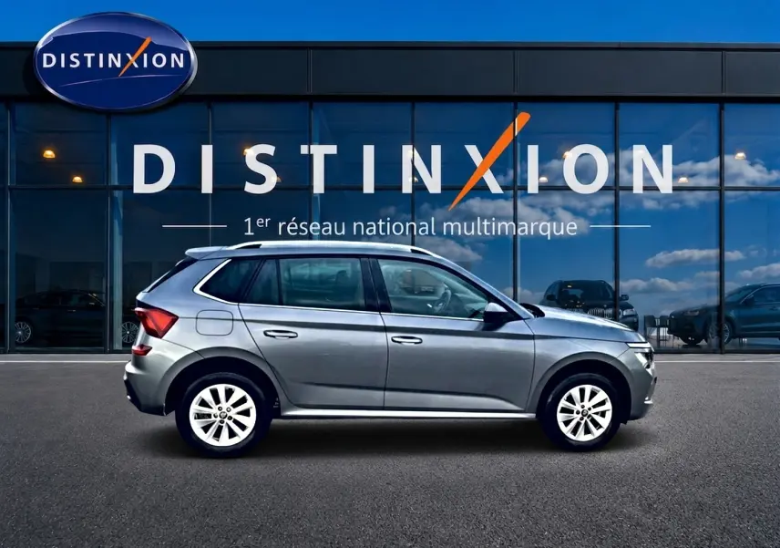 Vue de profil côté gauche d'un Skoda Kamiq gris 2025 garé devant une vitrine avec logo Distinxion.
