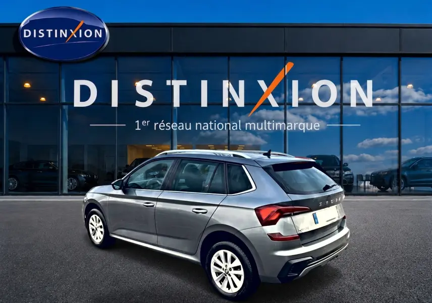 SKODA KAMIQ gris en 3/4 arrière droit, avec barres de toit et jantes alu blanches, devant une vitrine Distinxion.