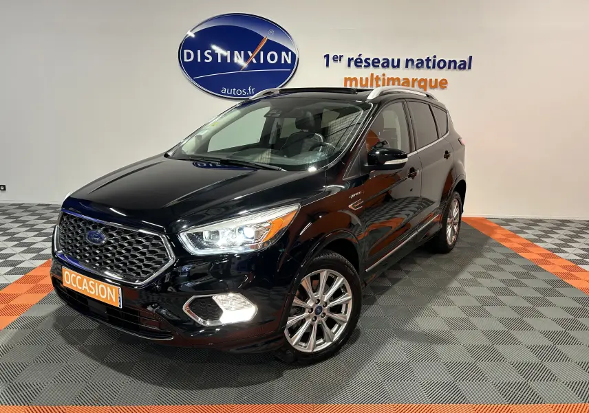 Ford Kuga noir en 3/4 avant droit, avec calandre hexagonale et feux LED allumés dans un showroom.