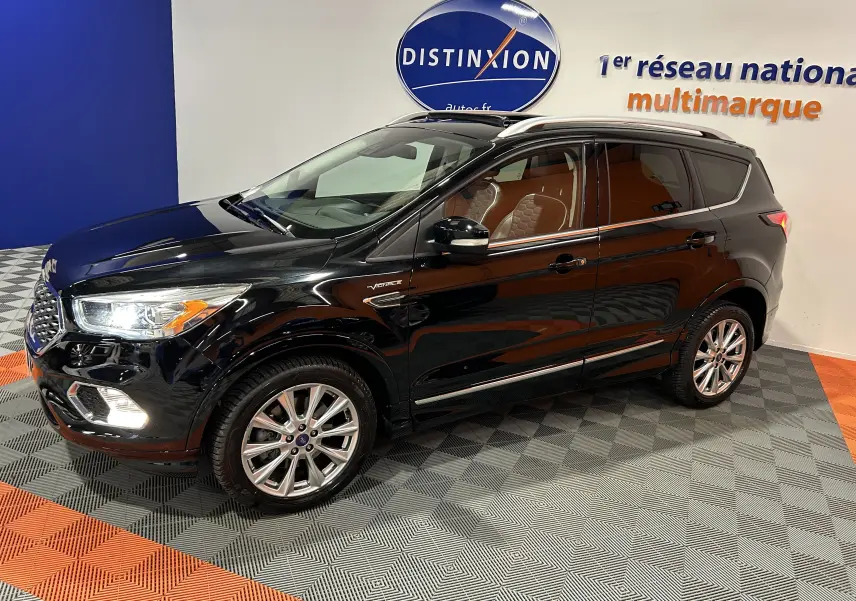 Ford Kuga Vignale noir en 3/4 avant droit, intérieur cuir clair et jantes alliage visibles en showroom.