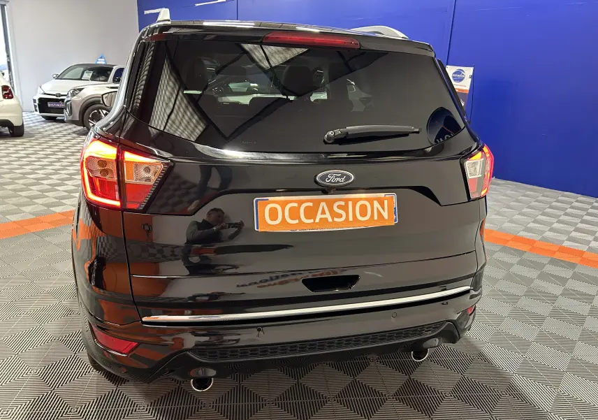 Vue arrière d'un Ford Kuga noir avec feux allumés et plaque "OCCASION" en intérieur showroom.