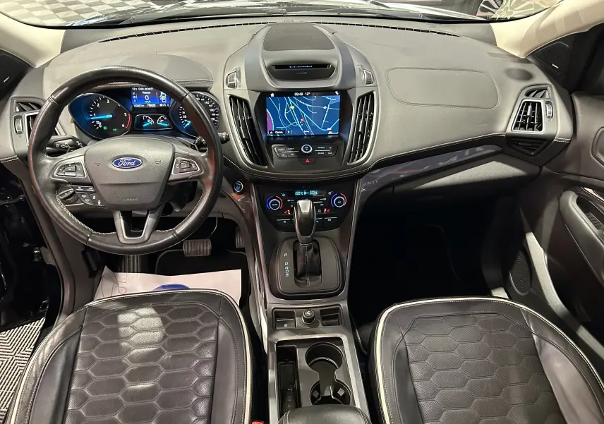 Vue intérieure avant du Ford Kuga noir 2017, tableau de bord avec écran tactile et volant cuir multifonction.