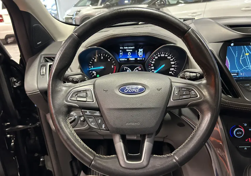 Vue intérieure centrée sur le volant noir en cuir du Ford Kuga 2017 avec tableau de bord et écran multimédia visible.