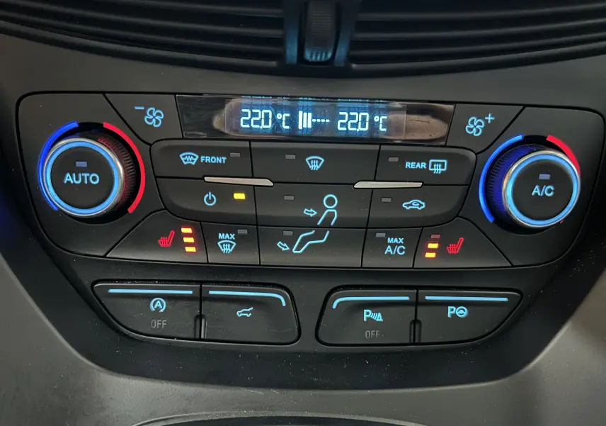 Gros plan sur la console de climatisation digitale du Ford Kuga noir, avec réglages chauffants et affichage à 22°C.
