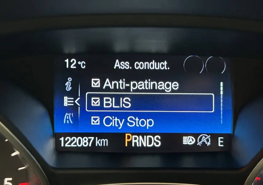 Affichage numérique du tableau de bord du Ford Kuga noir, montrant les aides à la conduite activées à 12°C.