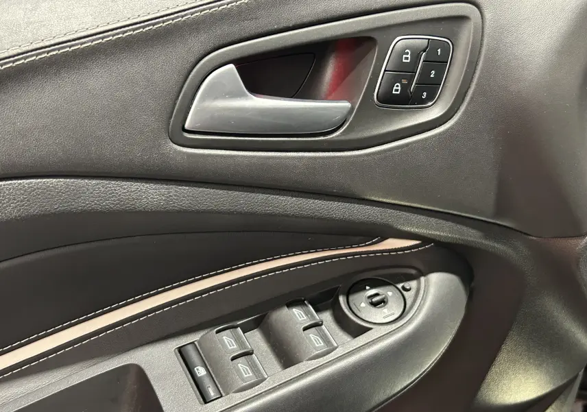 Gros plan sur la porte côté gauche du Ford Kuga noir, montrant la poignée intérieure et les commandes électriques des vitres.