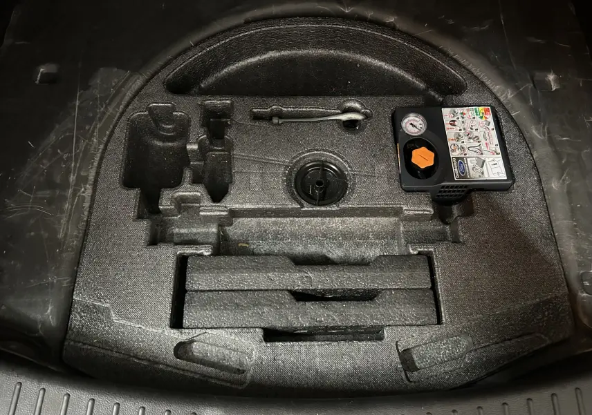 Vue en plongée du compartiment de rangement noir sous le coffre du Ford Kuga 2017, avec kit de réparation pneus intégré.