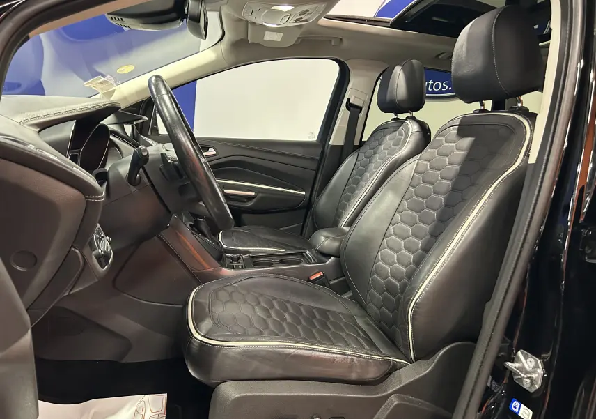 Vue intérieure côté conducteur du Ford Kuga noir 2017, sièges cuir noirs avec surpiqûres blanches et toit ouvrant panoramique.