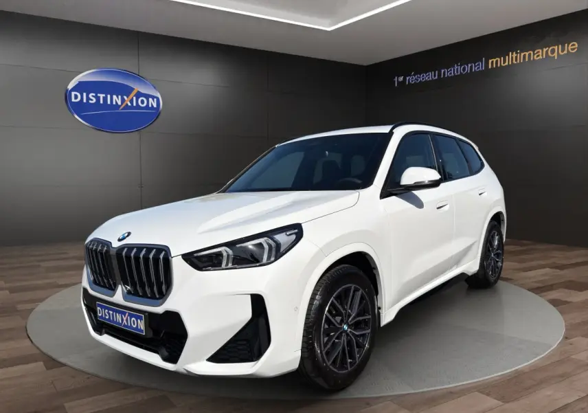 BMW X1 sDrive20d blanc vue 3/4 avant droit en showroom avec calandre noire et jantes foncées.