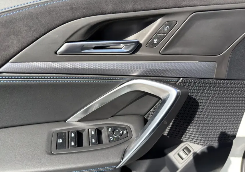 Détail de la porte avant gauche de BMW X1 blanc, avec commandes de vitres et poignée argentée.