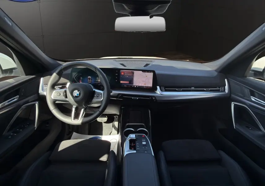 Vue intérieure avant de la BMW X1 sDrive20d 2025, tableau de bord moderne avec écran tactile et volant multifonction en cuir.